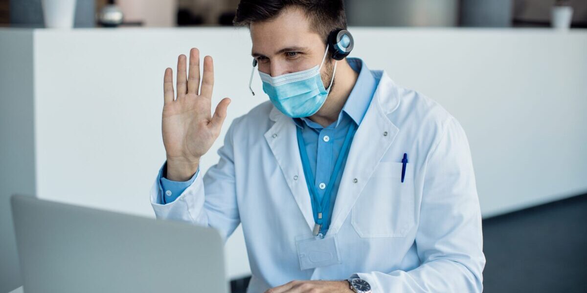 Male doctor waving during a video call over laptop at medical c Telemedicine, Healthcare