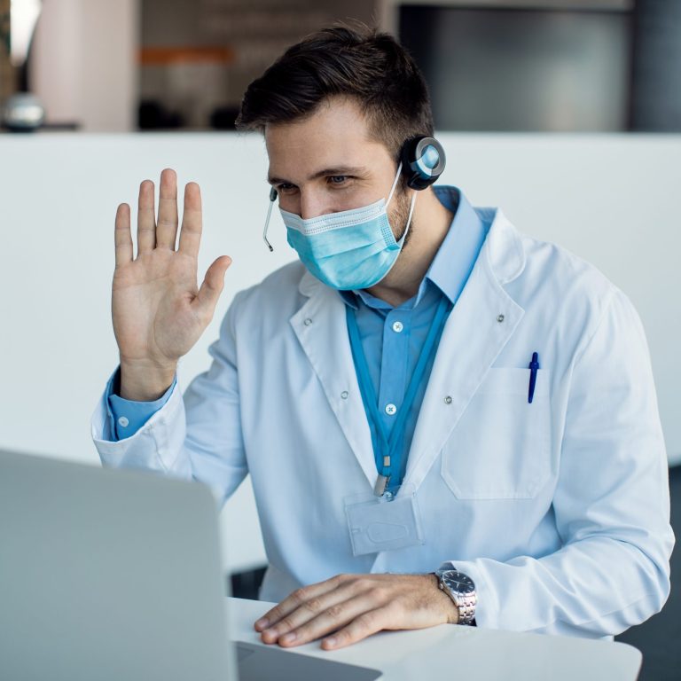 Male doctor waving during a video call over laptop at medical c Telemedicine, Healthcare