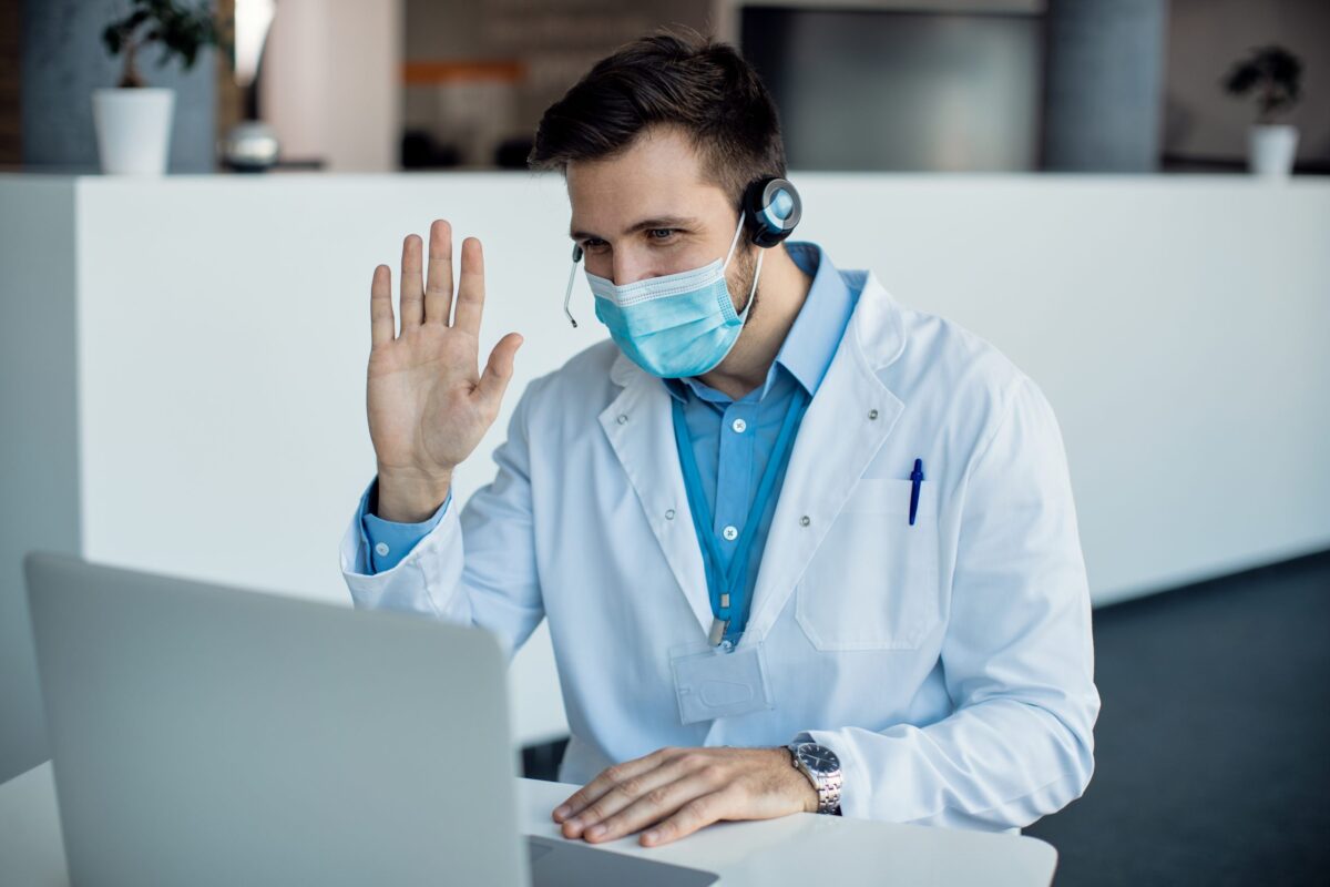 Male doctor waving during a video call over laptop at medical c Telemedicine, Healthcare